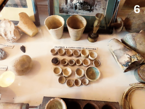 Instrumentos de laboratorio de ensayo (assay office) originales, utilizados para averiguar cuánto oro y plata contenía una muestra de mineral, una información decisiva para saber si una veta merecía ser explotada. Los recipientes grandes de la parte superior son crisoles (“crucibles”), en los que se calentaba mineral pulverizado mezclado con fundentes y compuestos de plomo; los pequeños recipientes alineados debajo son copelas (“cupels”), fabricadas tradicionalmente con un material muy poroso —frecuentemente ceniza de hueso— capaz de absorber el óxido de plomo durante la copelación. El oro y la plata quedaban finalmente concentrados en una diminuta perla metálica que podía pesarse y analizarse, decidiendo así si la veta merecía ser explotada o no. Estos instrumentos se encuentran en Bodie, un “pueblo fantasma” de la fiebre del oro de California, expuestos como curiosidad. Hoy en día, la mina de Bodie ha vuelto a funcionar, y se extrae oro mediante técnicas no tan diferentes de las de hace 200 años. (Haffty, Riley y Goss, 1977). (FA)
REFERENCIAS DEL APARTADO 06
• Haffty, J., Riley, L. B., y Goss, W. D. (1977). A manual on fire assaying and determination of the noble metals in geological materials (U.S. Geological Survey Bulletin 1445). U.S. Government Printing Office. https://digital.library.unt.edu/ark:/67531/metadc1115061/